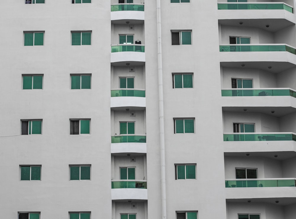 a tall white building with green windows and balconies