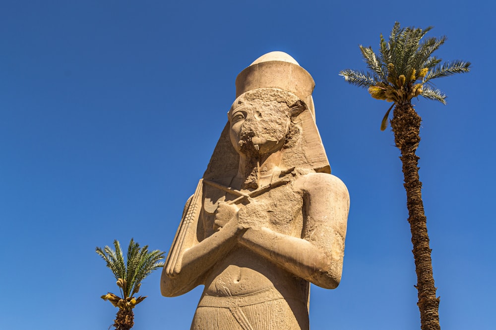 a statue of an egyptian woman with a palm tree in the background
