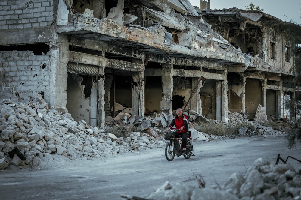 a person riding a bike in front of a destroyed building