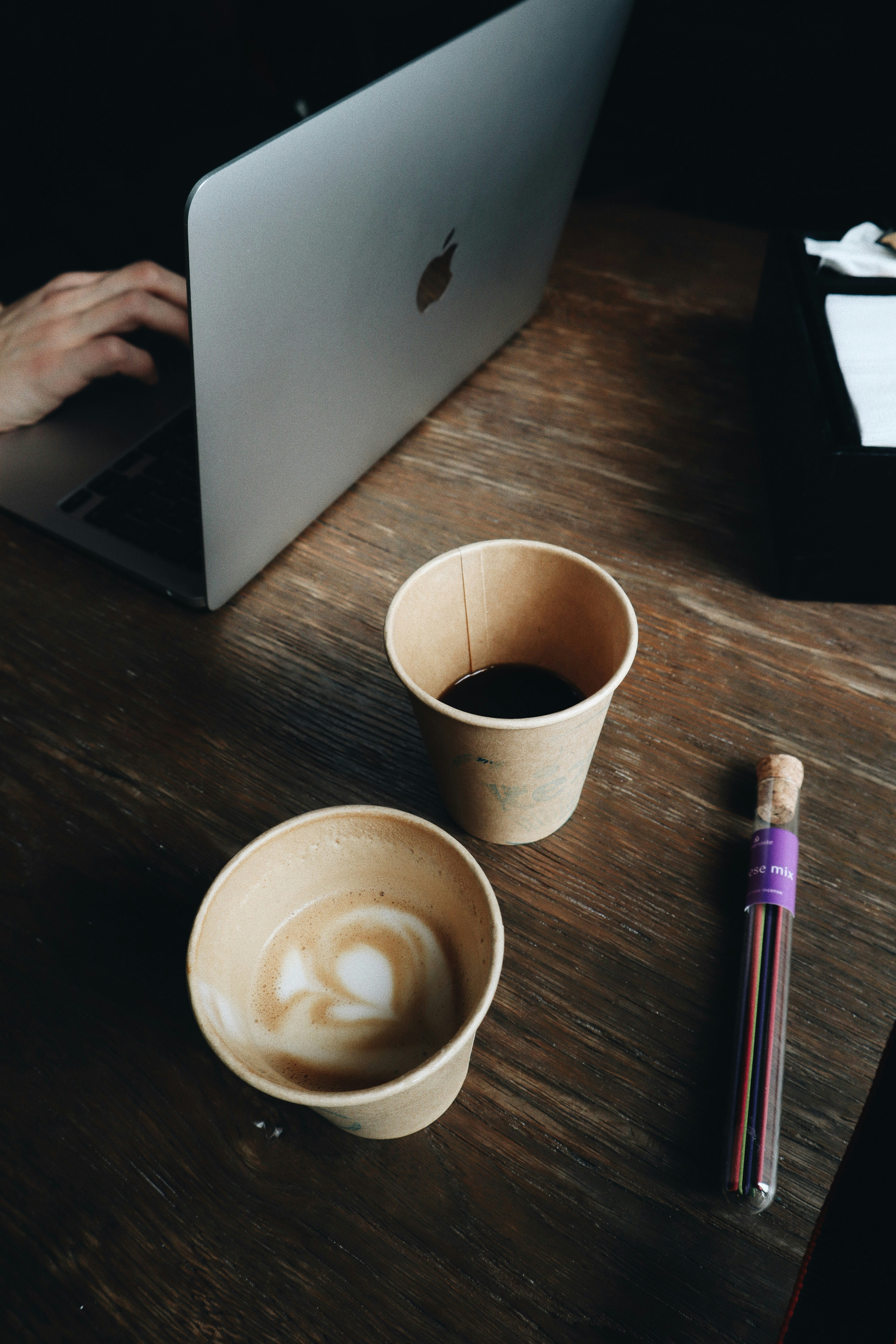 Close-up of hands typing on a laptop with academic papers and a coffee cup nearby.