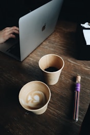 A person typing on a laptop with a notebook and coffee nearby.