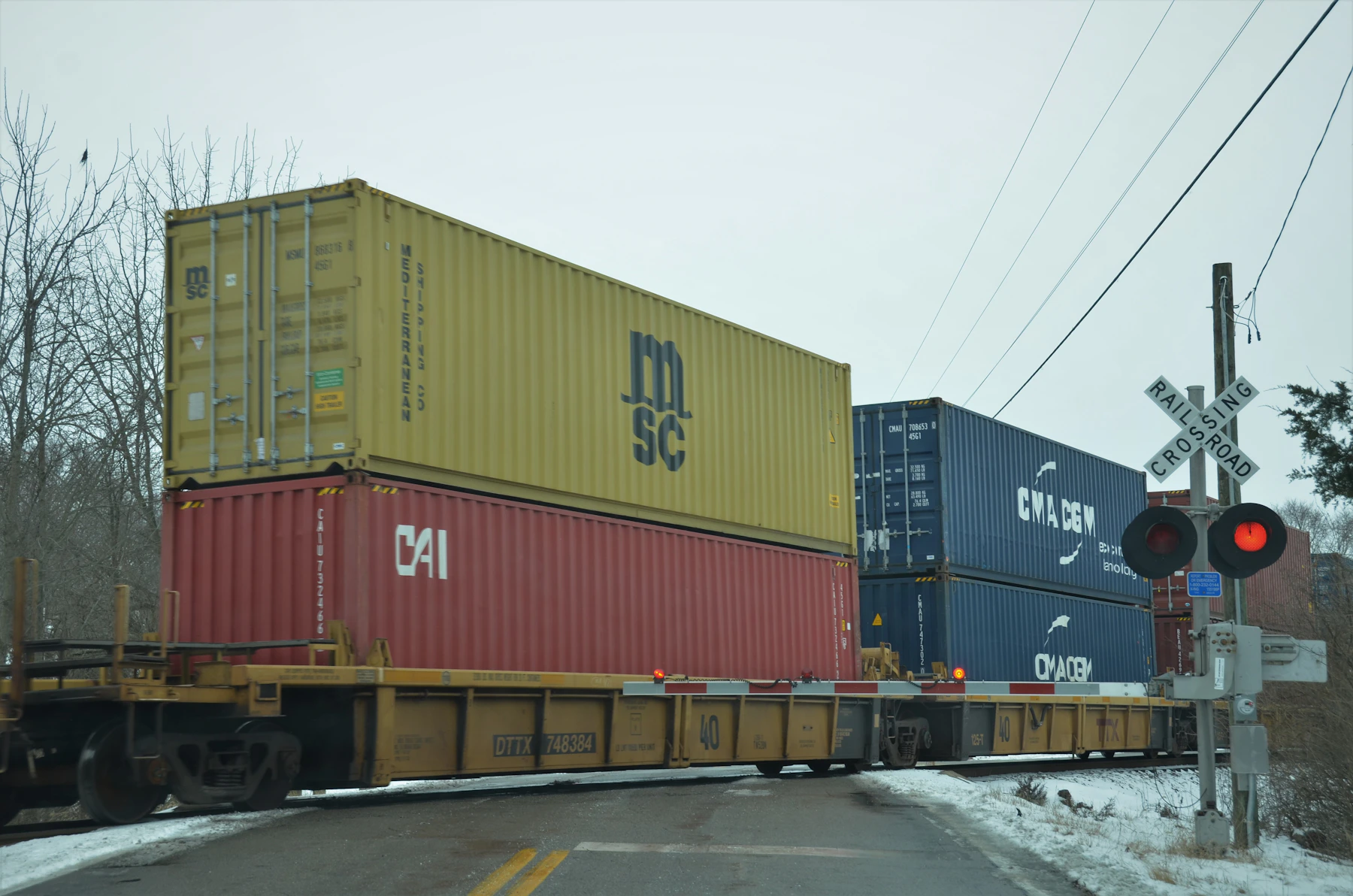A doublestack intermodal container train carrying MSC, CAI and China Shipping containers across a railroad crossing