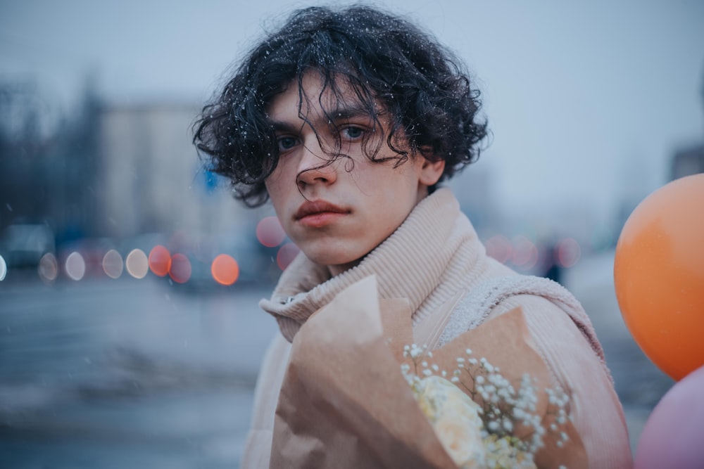 a man with curly hair and a turtle neck sweater standing in front of balloons