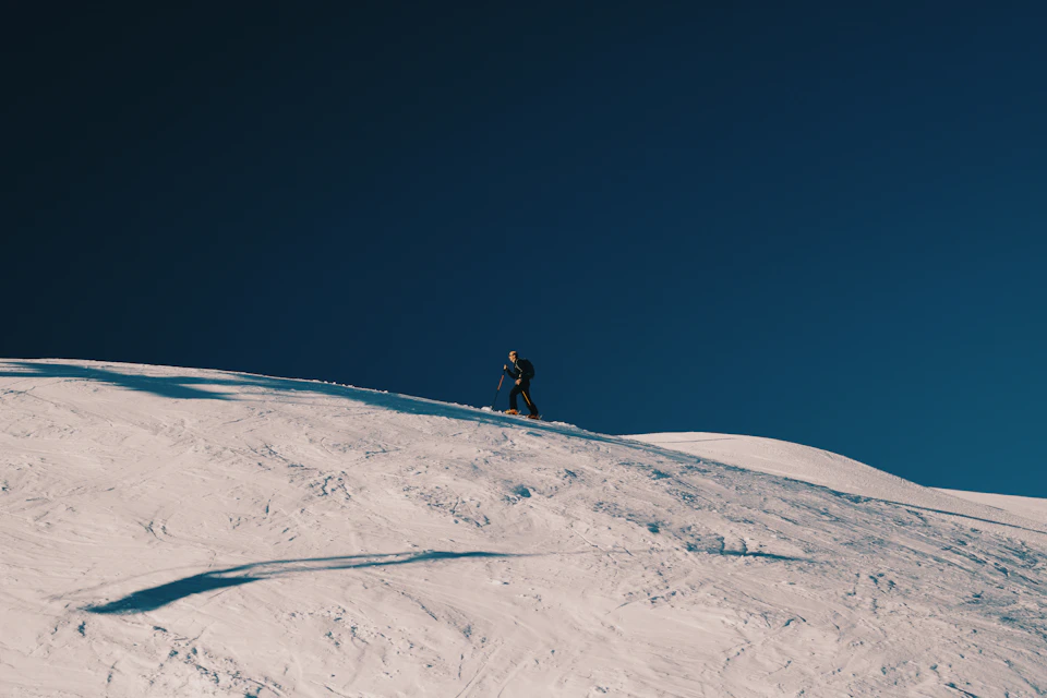 Lone skier navigates snowy mountain slope under clear blue sky with black clothing