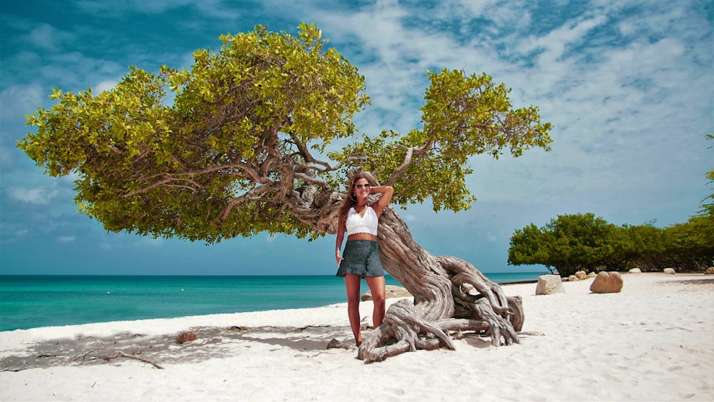 a woman standing next to a tree on a beach