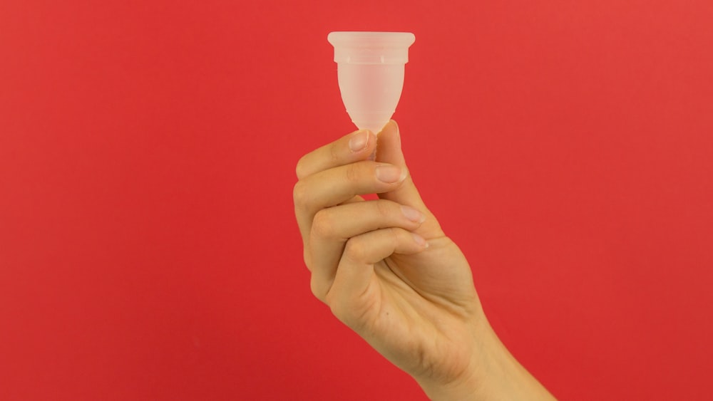 una mano che tiene un piccolo bicchiere di plastica davanti a uno sfondo rosso