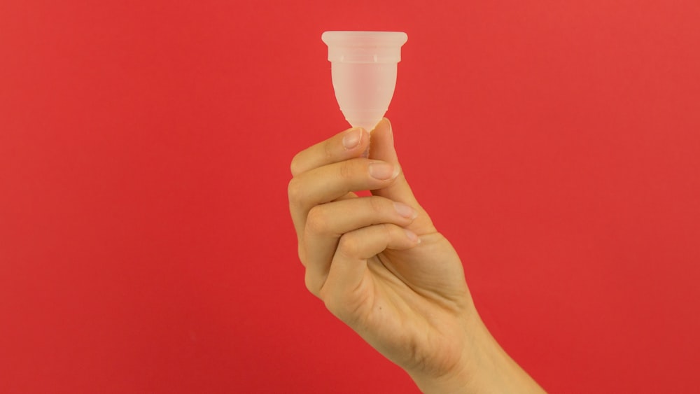 a hand holding a small plastic cup in front of a red background
