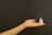 A human hand with an extended palm is holding a small, transparent menstrual cup against a plain, dark background.