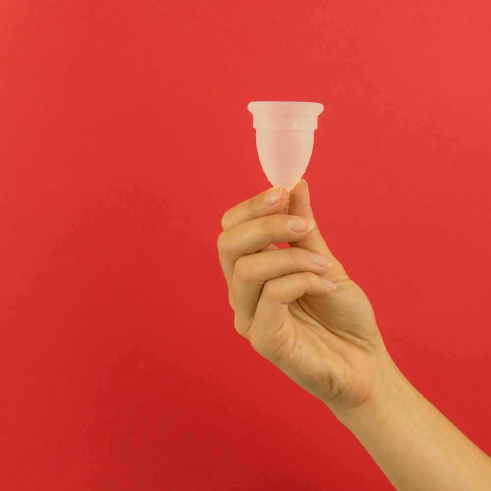 a hand holding a plastic cup on a red background