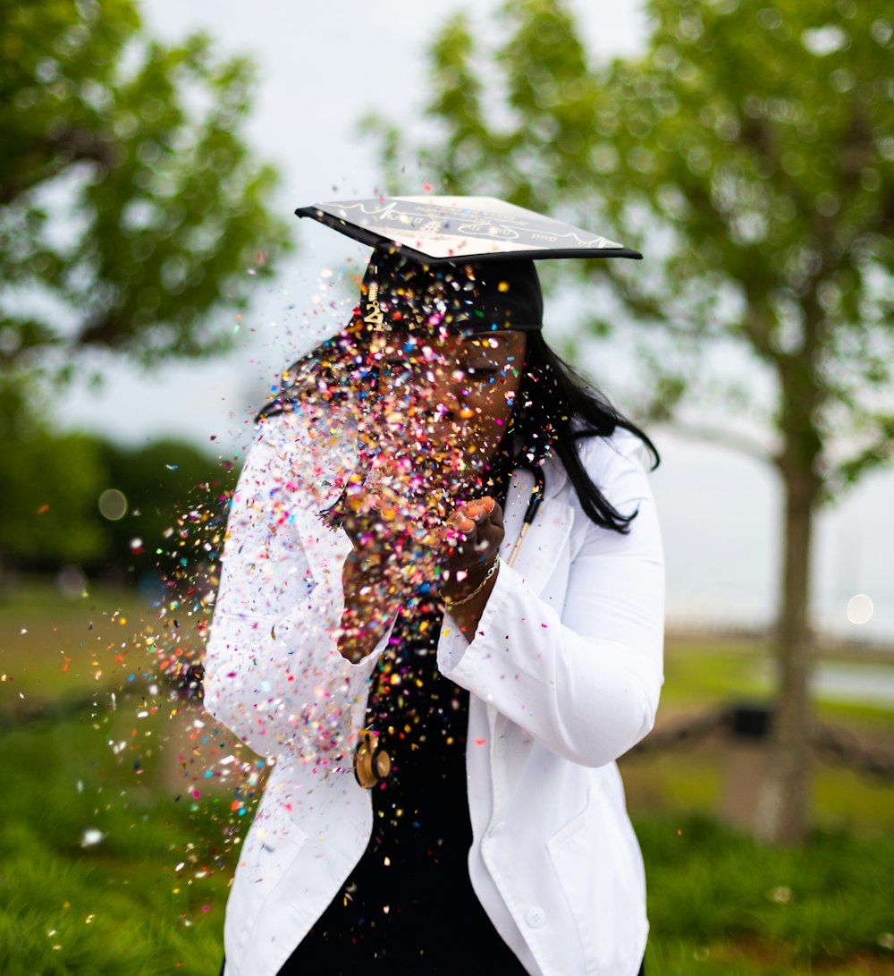 Une femme portant une casquette de fin d’études lui jetant des confettis au visage