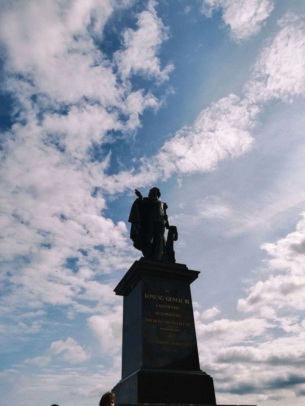 a man standing next to a statue under a cloudy blue sky