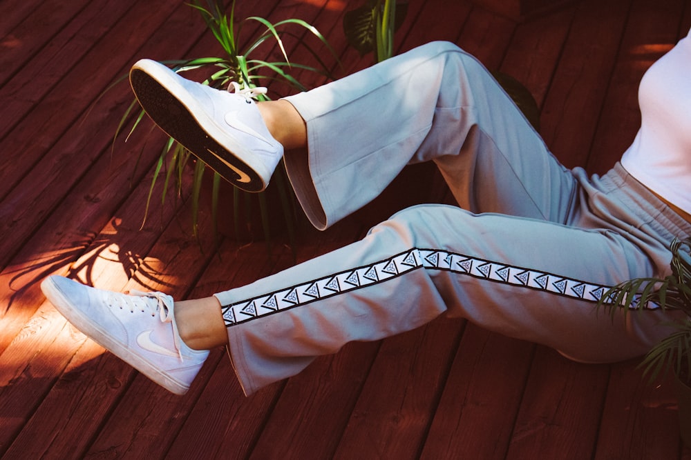 a person sitting on a wooden floor wearing white sneakers