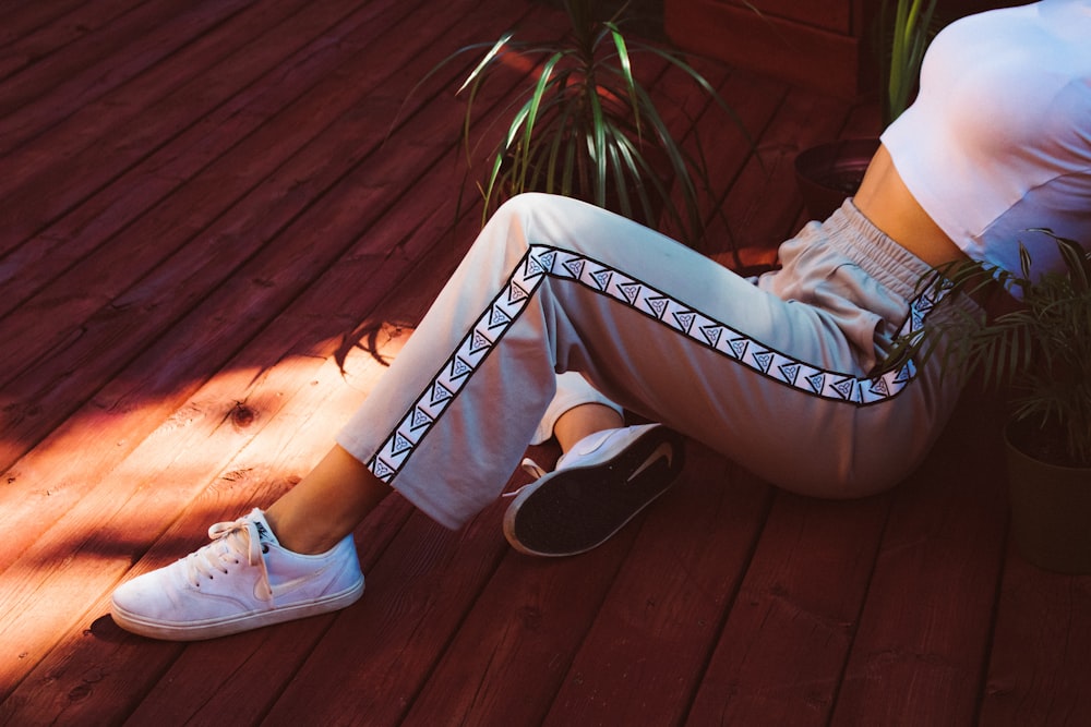 a woman sitting on a wooden floor wearing white sneakers