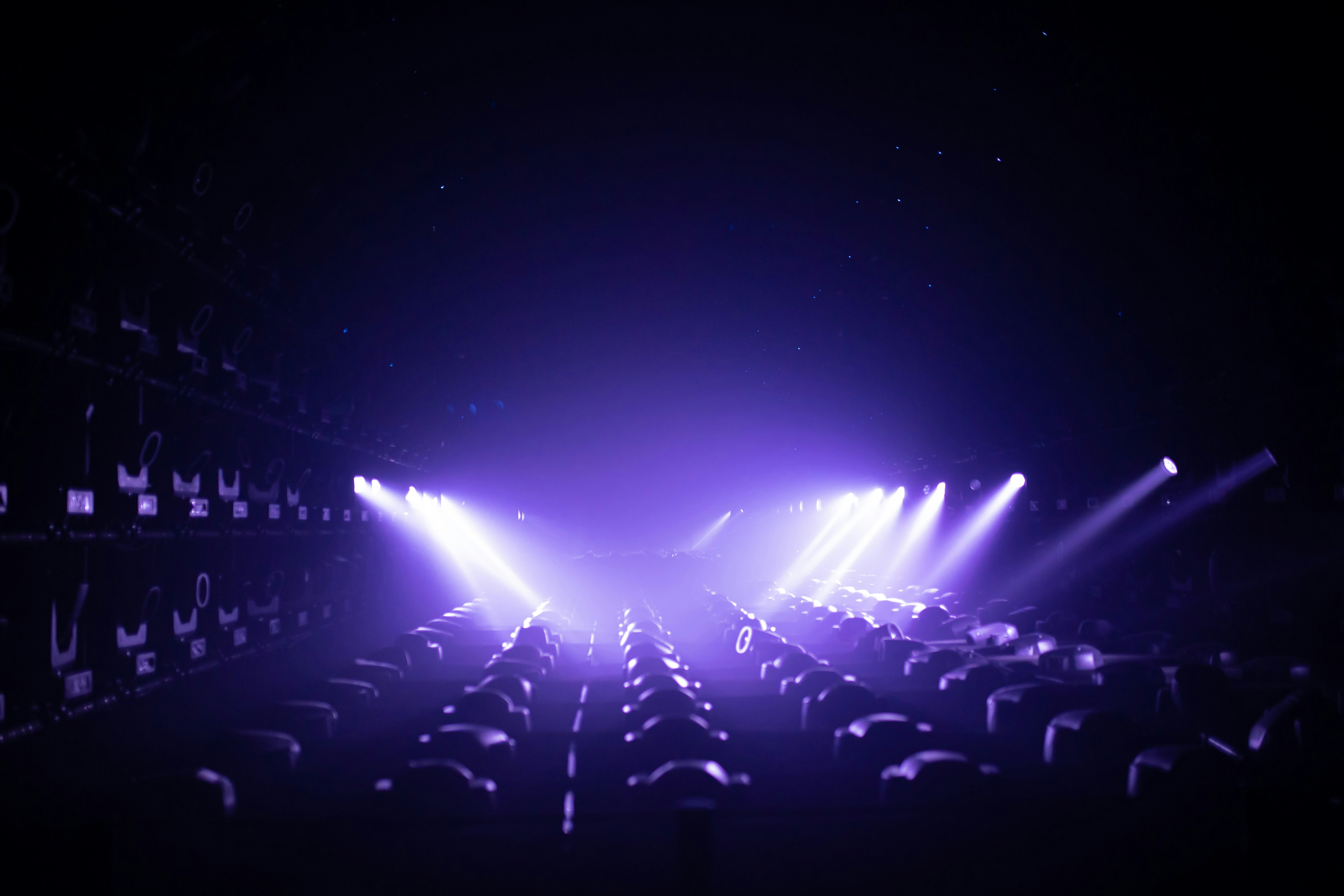 Empty concert hall with rows of dark seats and bright stage lights.