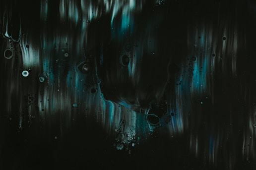 Dark abstract artwork featuring fluid, flowing patterns with subtle circular elements. Shades of deep green, black, and hints of teal or blue create a mysterious ambiance.