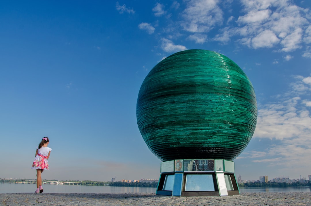 a woman standing in front of a large green object, Globe monument