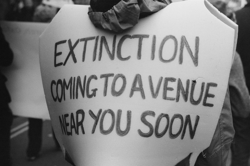 a person holding a sign that says, extinction coming to a venue near you soon
