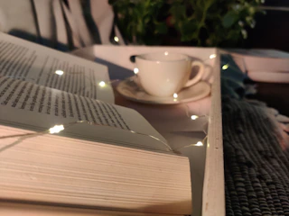 Softly glowing fairy lights twinkling above a stack of worn fantasy novels beside a steaming mug of tea.