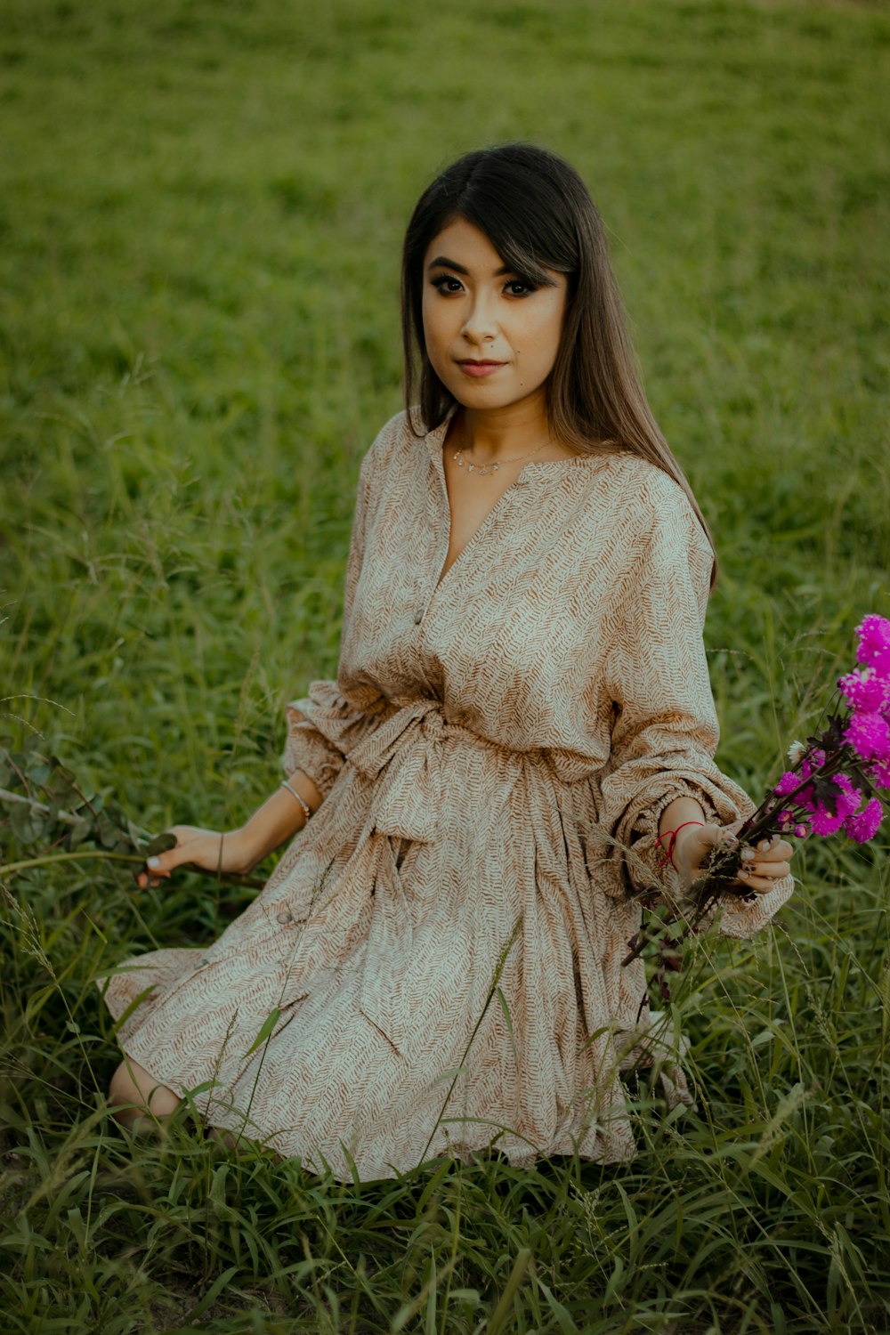 a young girl sitting in a field holding a purple flower