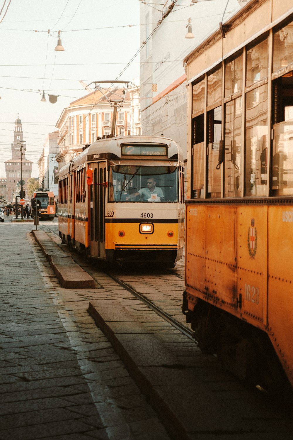 a yellow and white train traveling down a street next to tall buildings