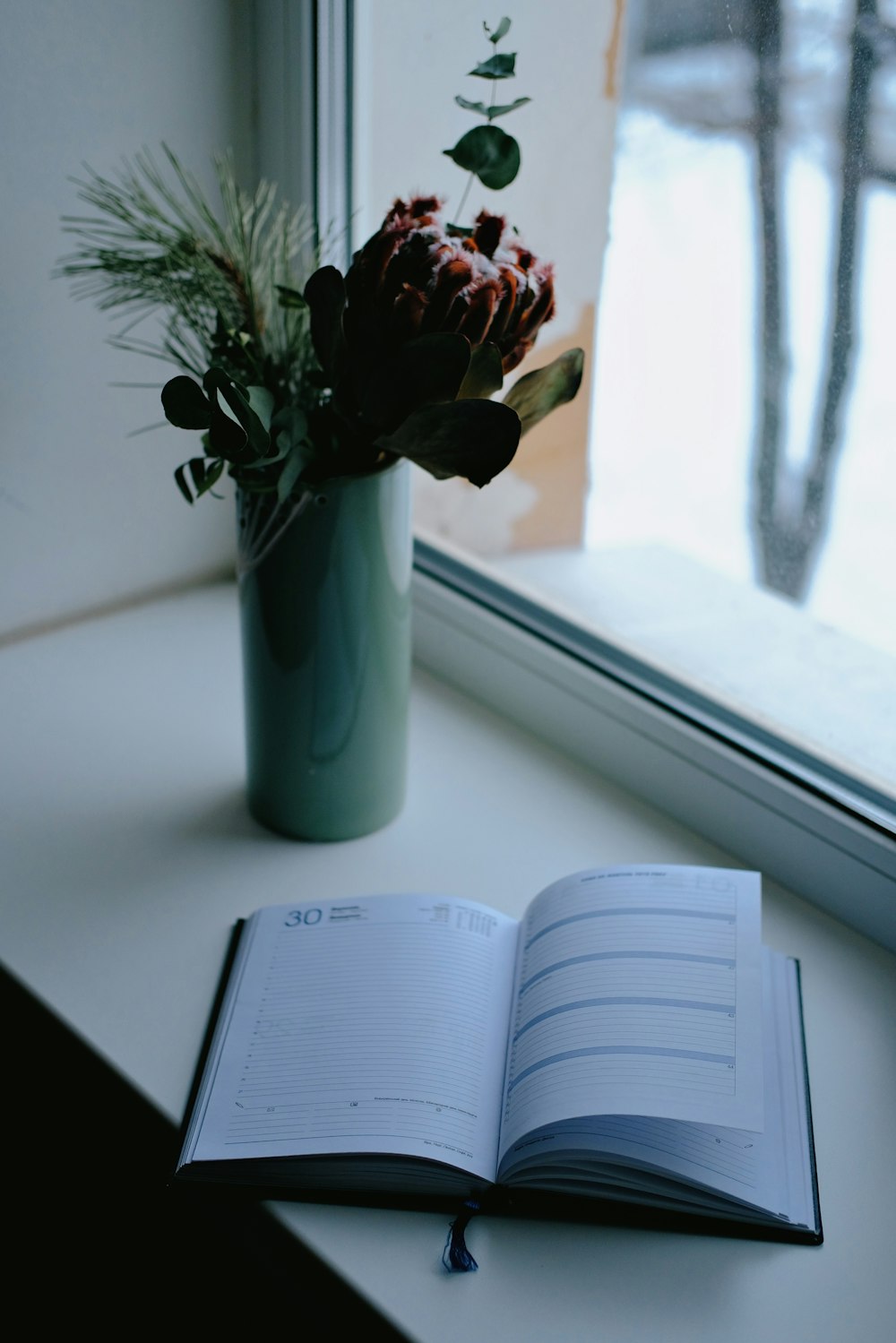 an open book sitting on top of a table next to a vase of flowers