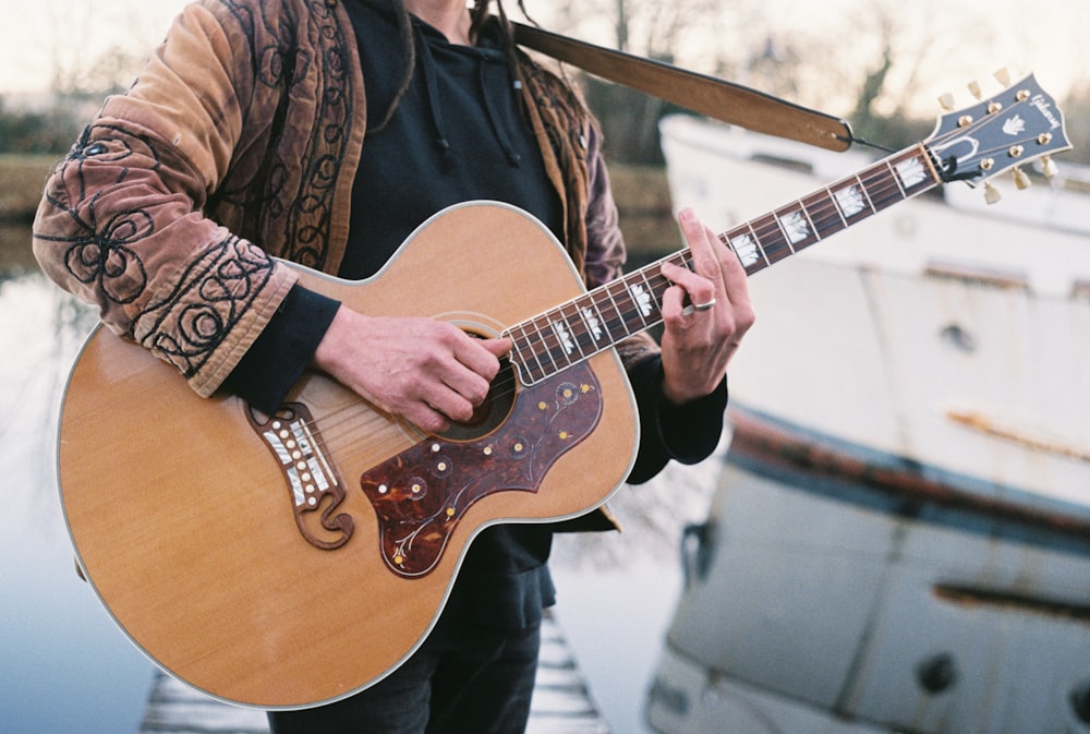 a man holding a guitar near a boat