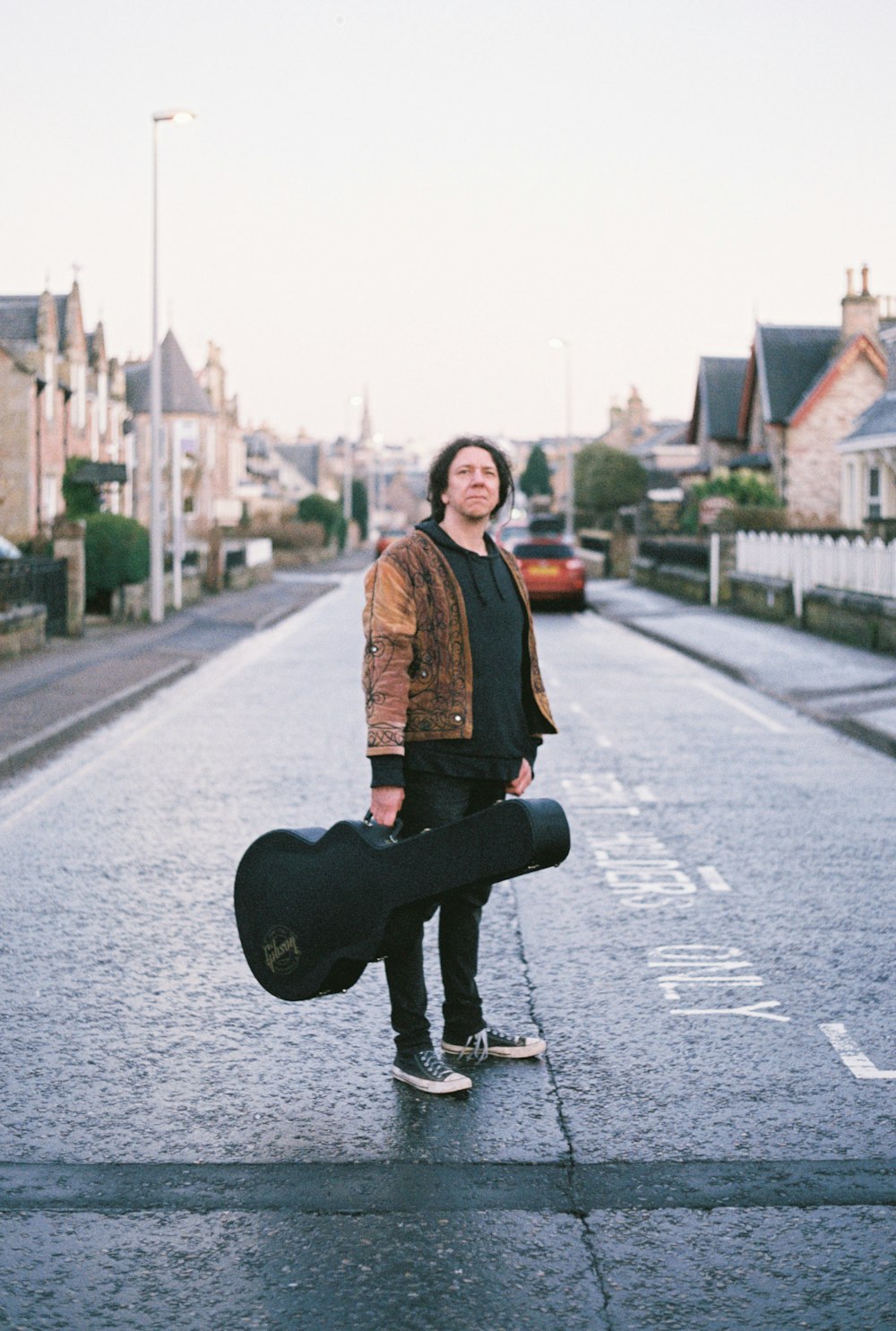 a man standing on the side of a road holding a guitar case