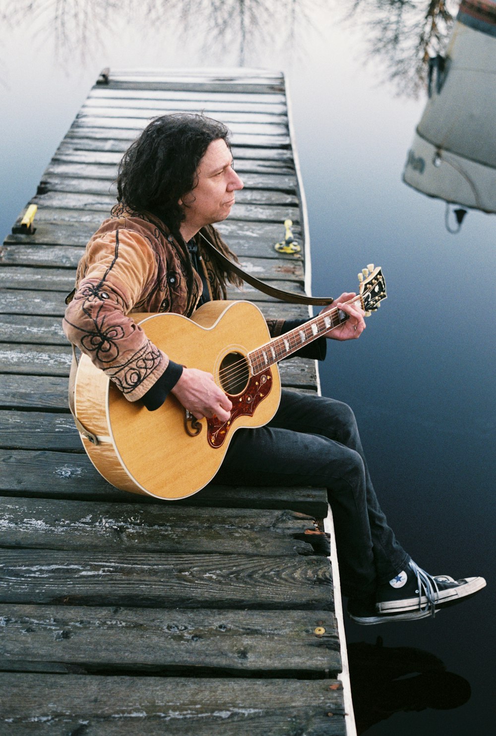 a man sitting on a dock playing a guitar