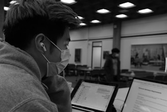a man wearing a face mask while looking at two laptops