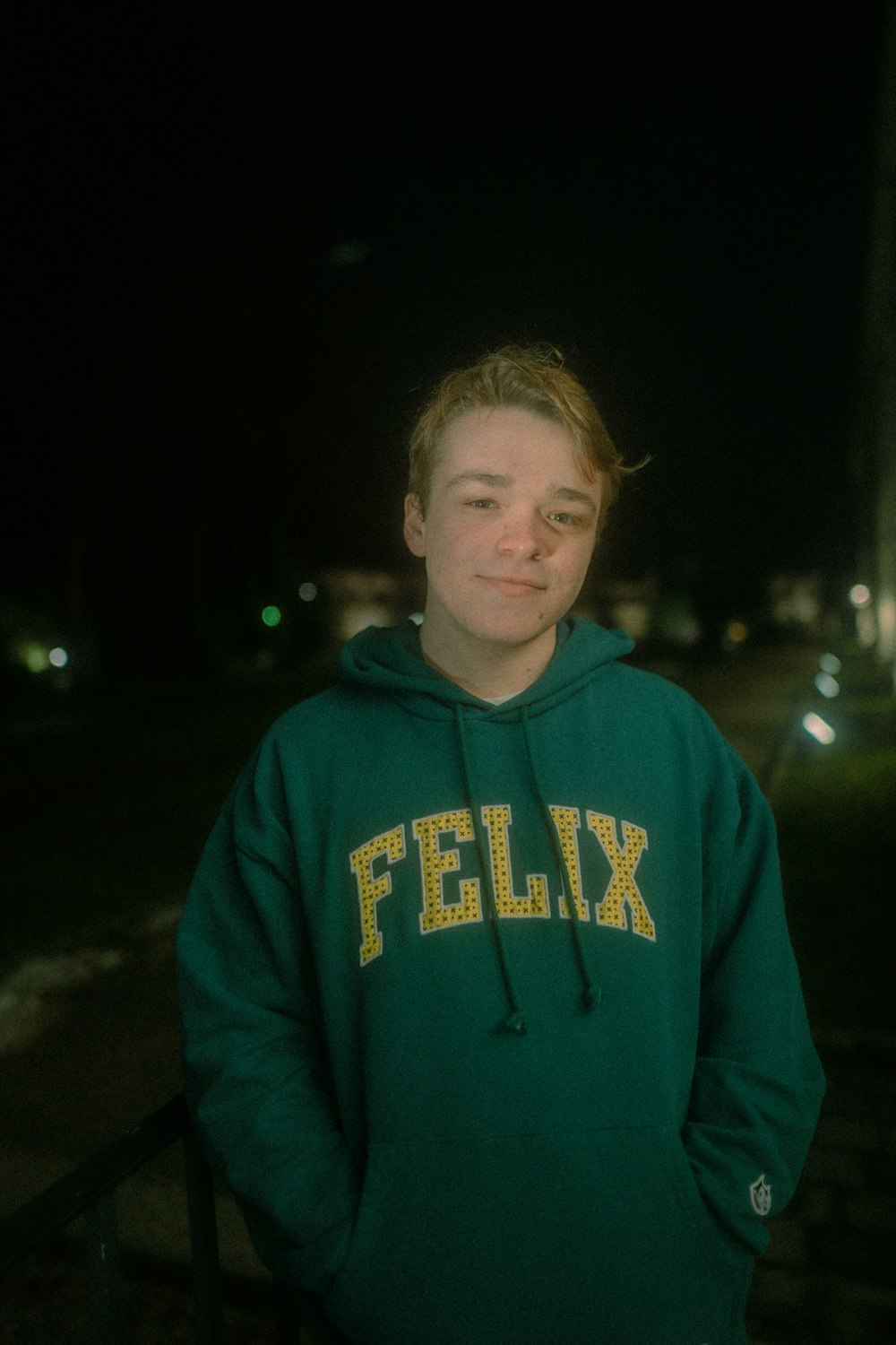 a young man in a green hoodie standing in front of a fence