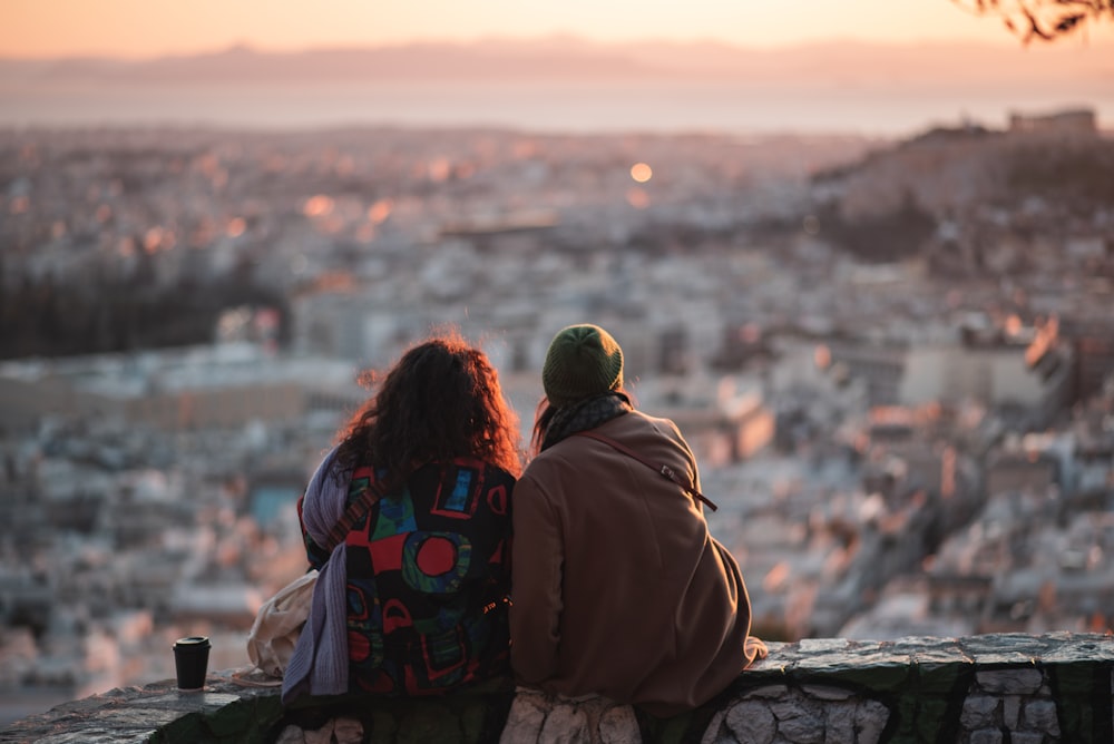 a couple of people sitting on top of a stone wall