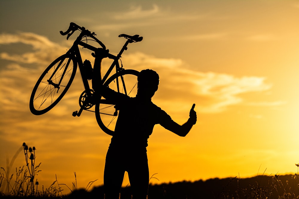 a silhouette of a man holding a bike on his shoulder