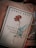 A book cover featuring the name Ahmed Arif at the top and a red carnation in the center. Below the flower, there is text in Turkish. A pair of light blue earphones is placed on the book, which rests on a soft fabric with a zippered section visible.