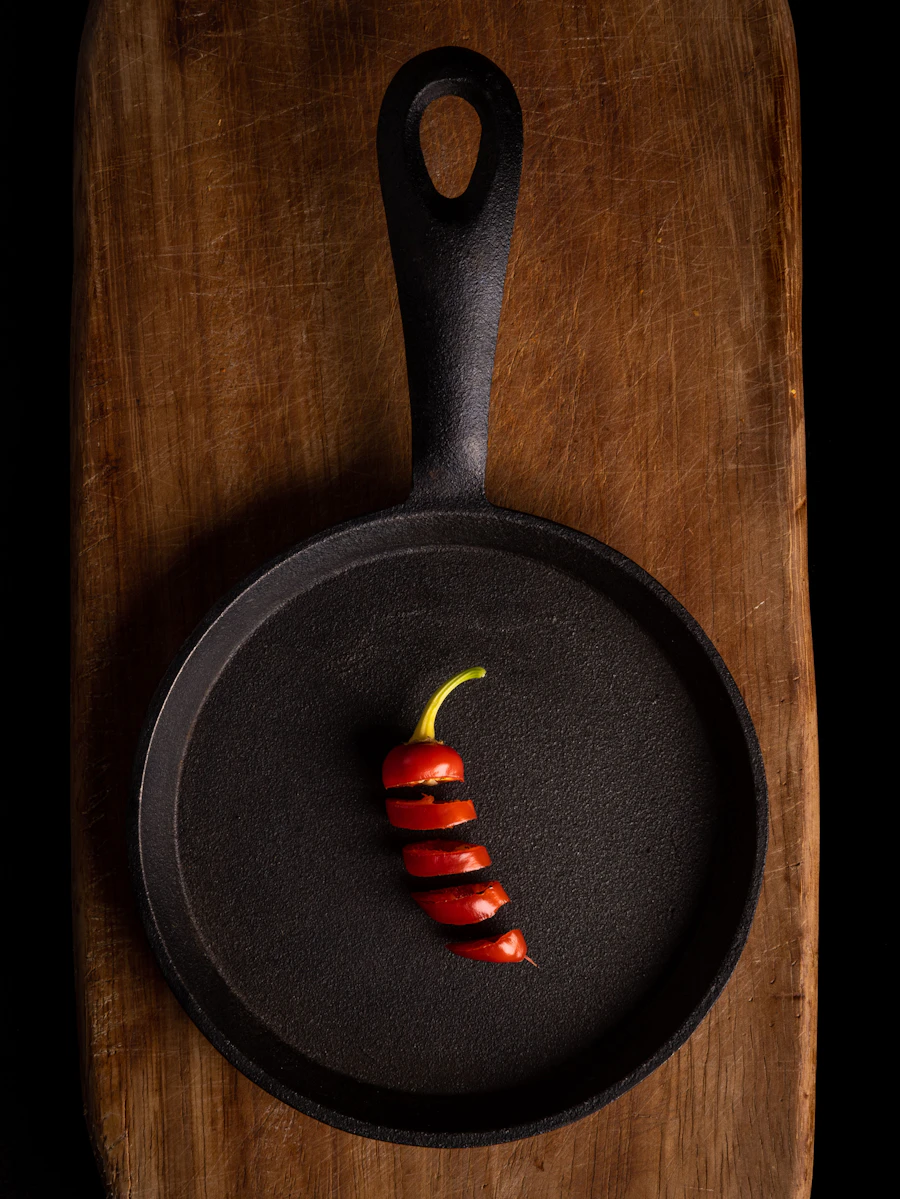 Small cast-iron skillet with a sliced red chili on a wooden plank against black