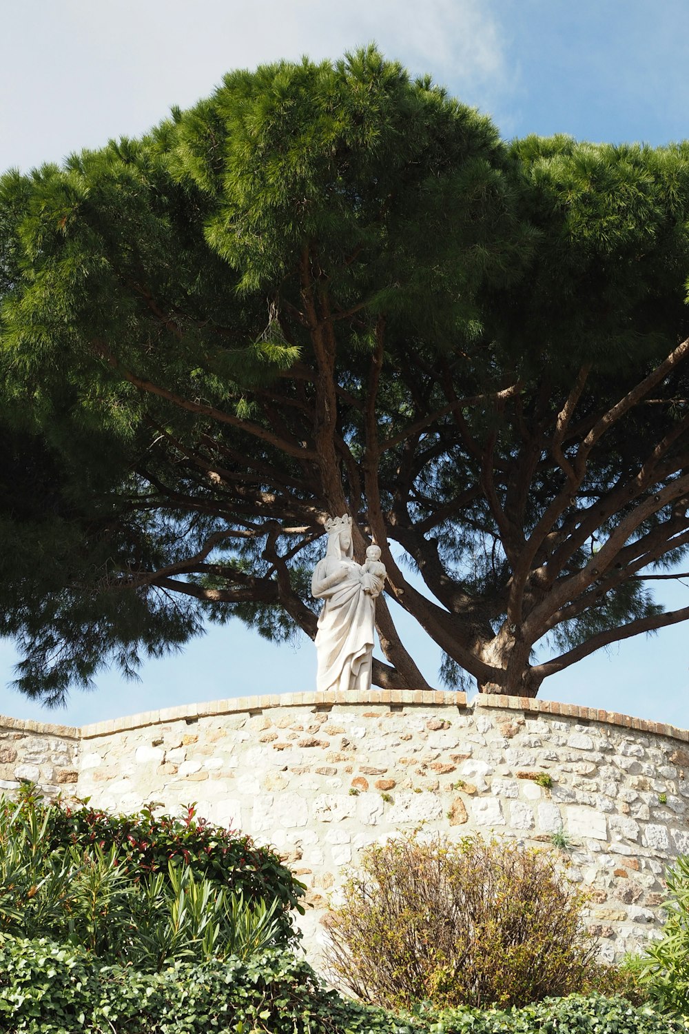 a statue sitting on top of a stone wall next to a tree