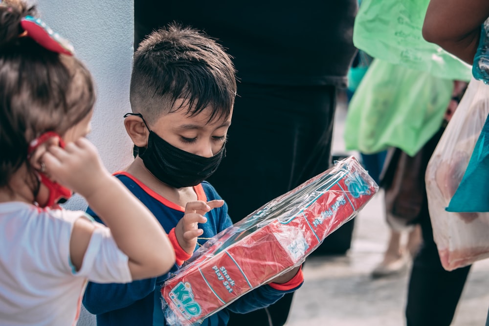 a little boy wearing a face mask and holding a box