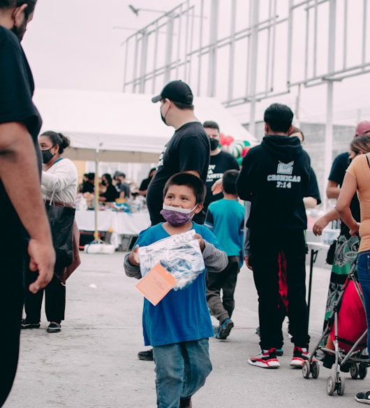 a young boy walking down a street next to a group of people