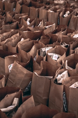 Numerous brown paper bags are arranged closely together in a densely packed manner. Some bags contain items that slightly protrude or are visible from the top.