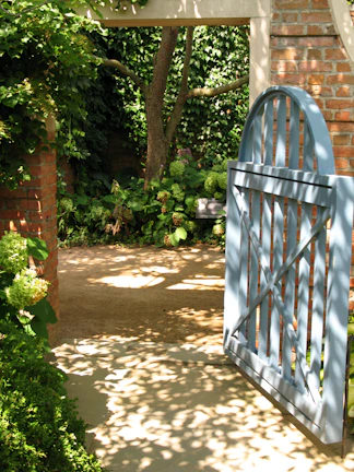 A sunlit garden gate framed by blooming roses and lush greenery.
