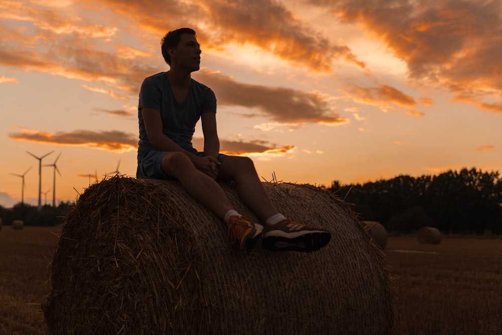 a man sitting on a bale of hay at sunset