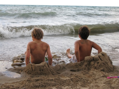 two boys sitting in the sand at the beach