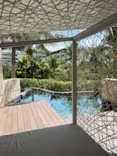 Wooden kiosk surrounded by lush greenery next to a sparkling community pool on a sunny summer day.
