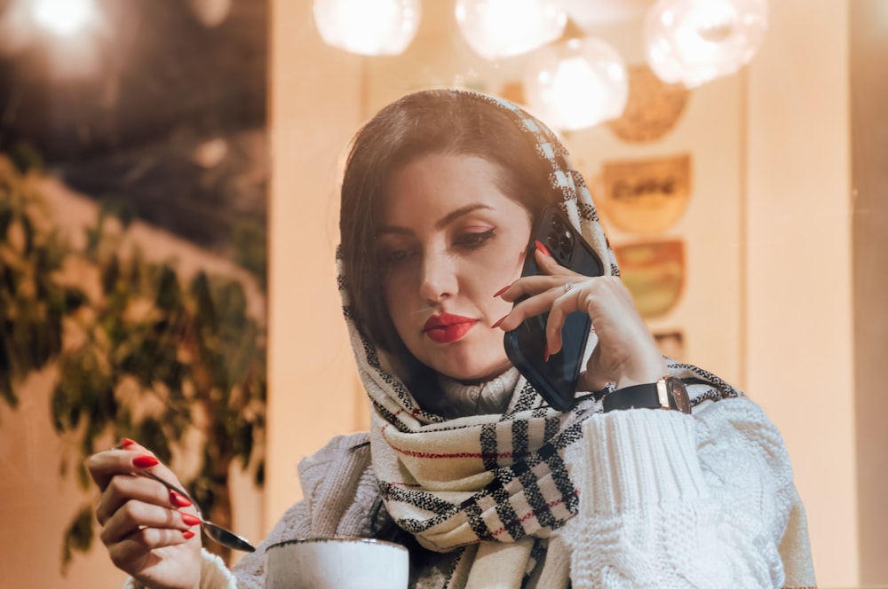 a woman talking on a cell phone while holding a cup of coffee