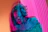 A double-exposed effect creates a dynamic and surreal impression with vibrant colors. A person with long hair wears glasses and a textured off-shoulder sweater. The backdrop consists of vertical pink neon lights, and the composition evokes a sense of futuristic, digital art.