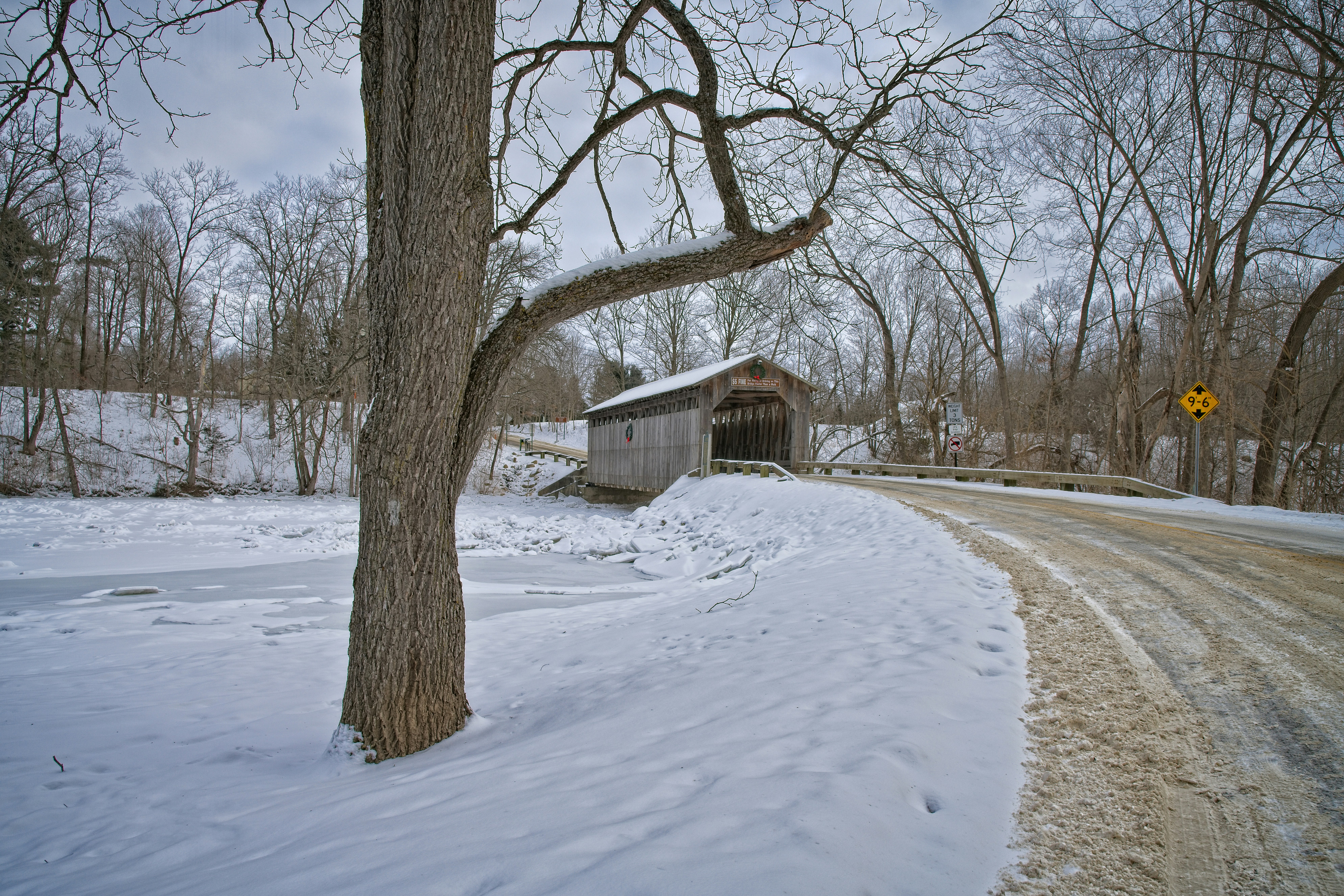 Holliwell Covered Bridge – a snow covered road next to a tree
