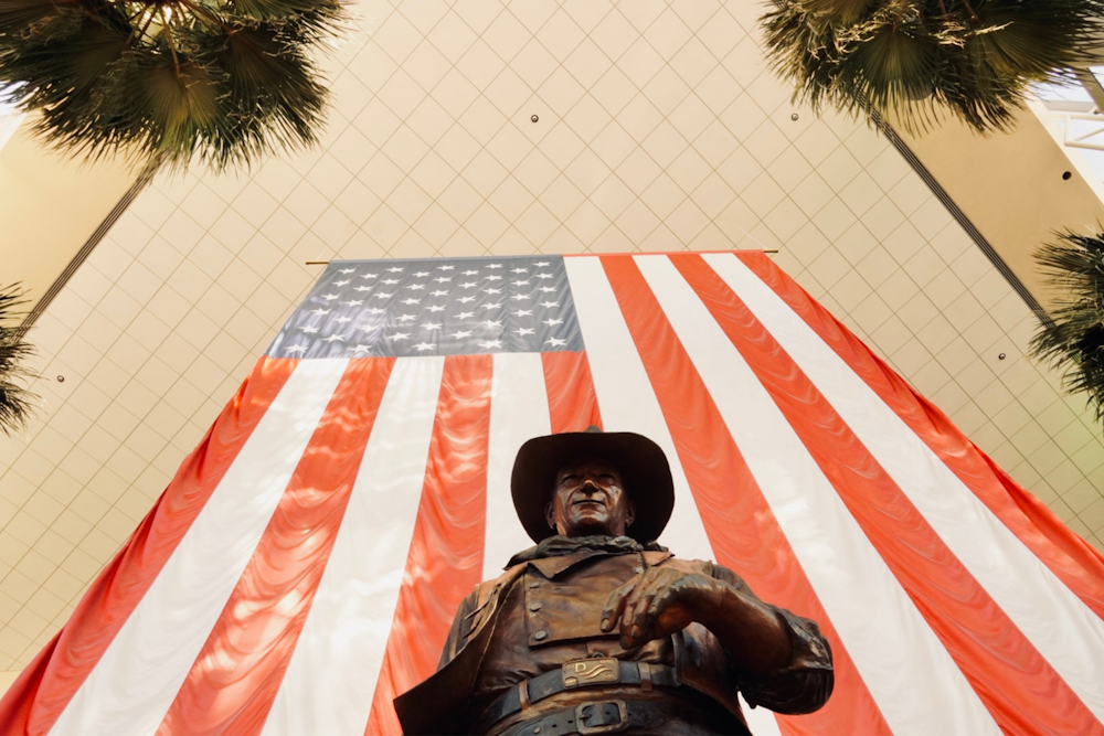 Una estatua de un hombre sosteniendo un arma frente a una bandera estadounidense