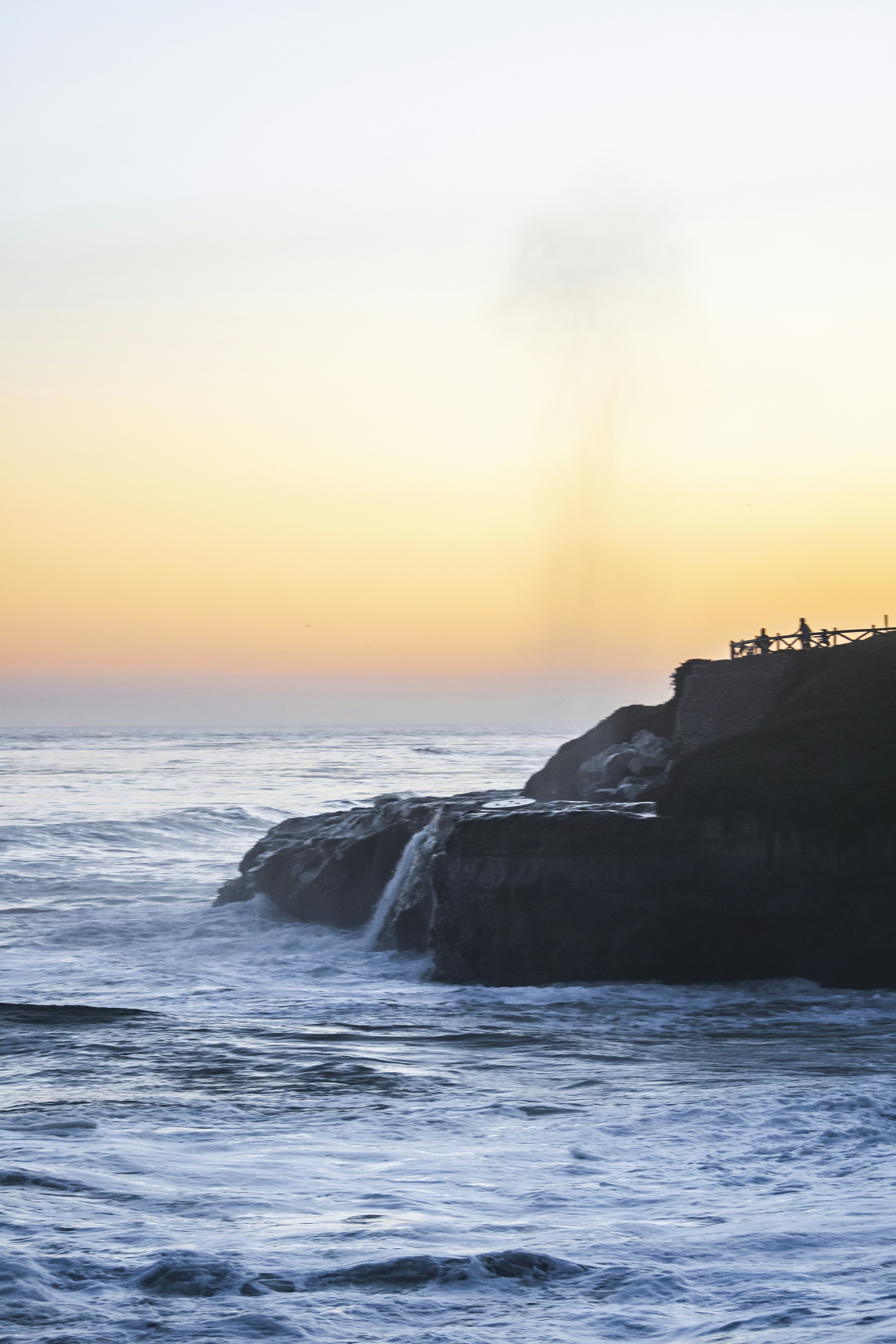 A couple of people standing on top of a cliff next to the ocean photo ...