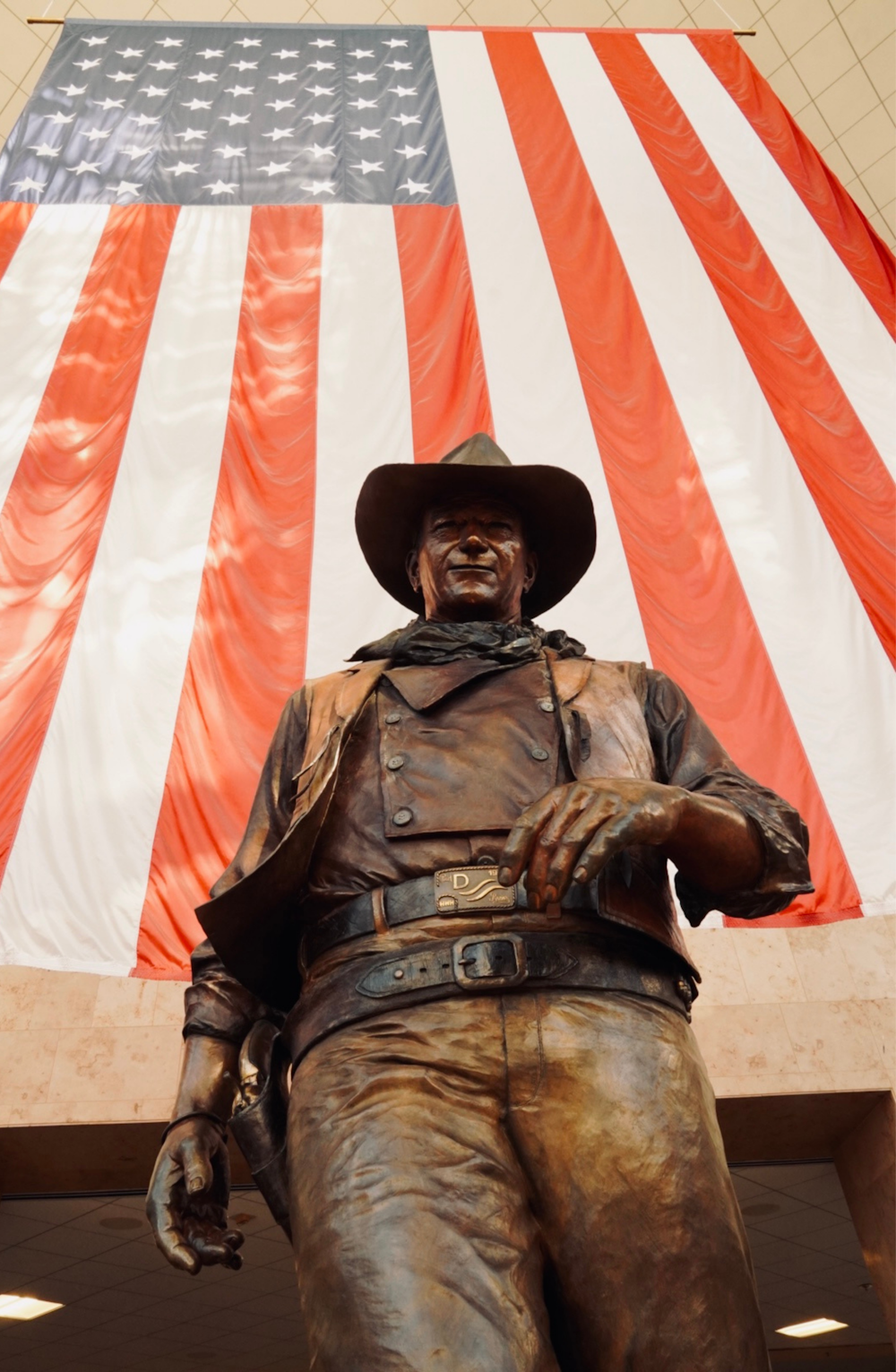 uma estátua de um homem em um chapéu de cowboy com uma bandeira americana no fundo