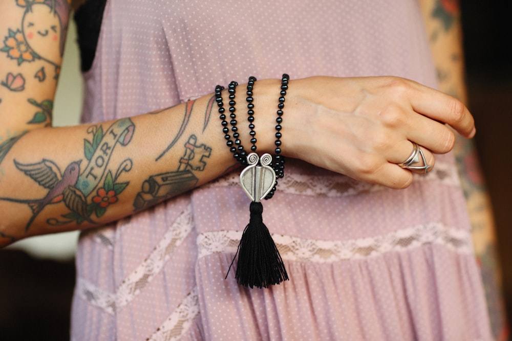 a woman with a tattoo on her arm wearing a tasseled necklace