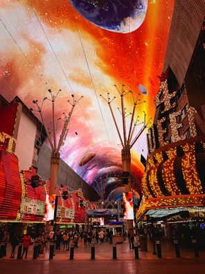 a brightly lit shopping mall with a colorful sky painted on the ceiling